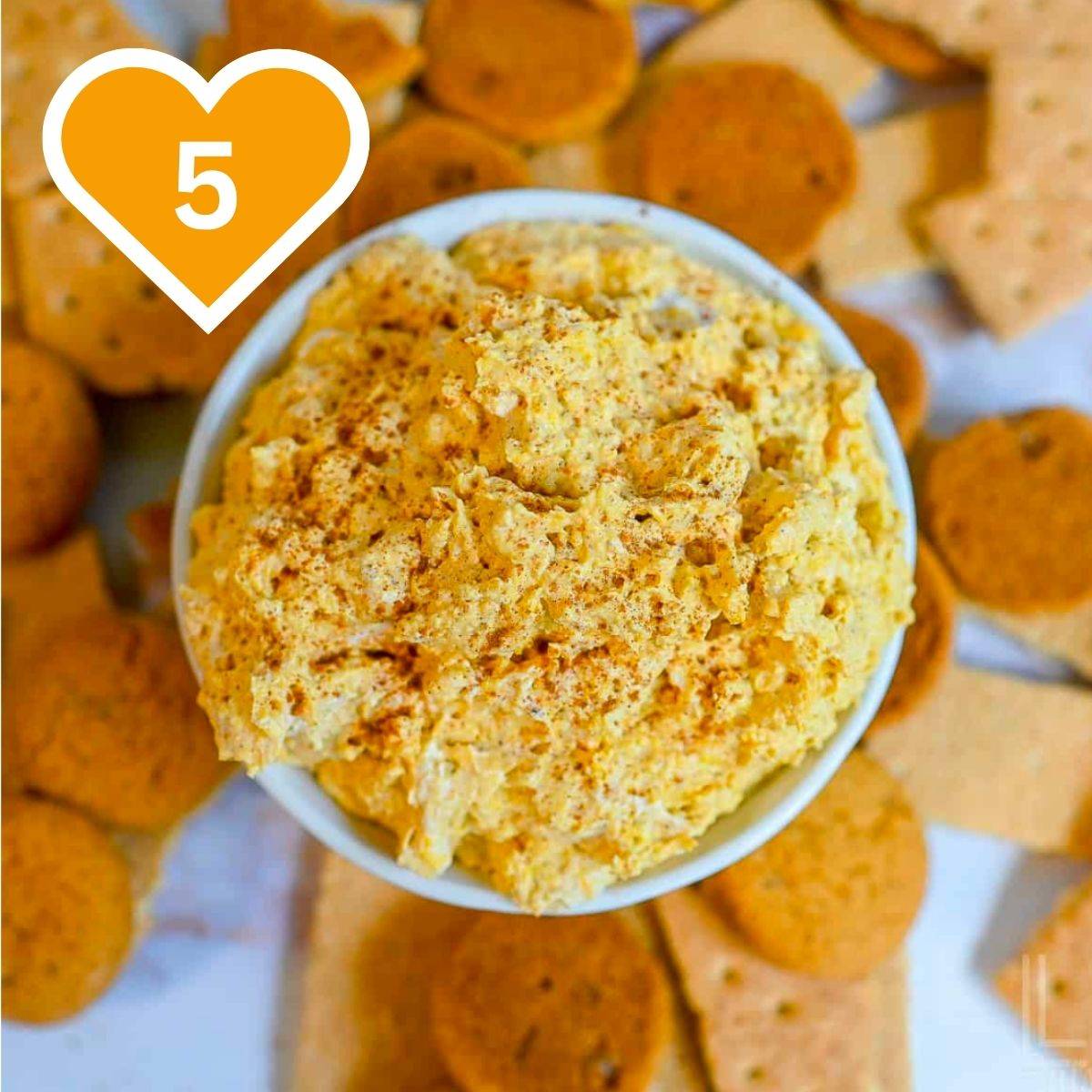 Bowl of creamy pumpkin fluff dip topped with cinnamon and surrounded by graham crackers for dipping.