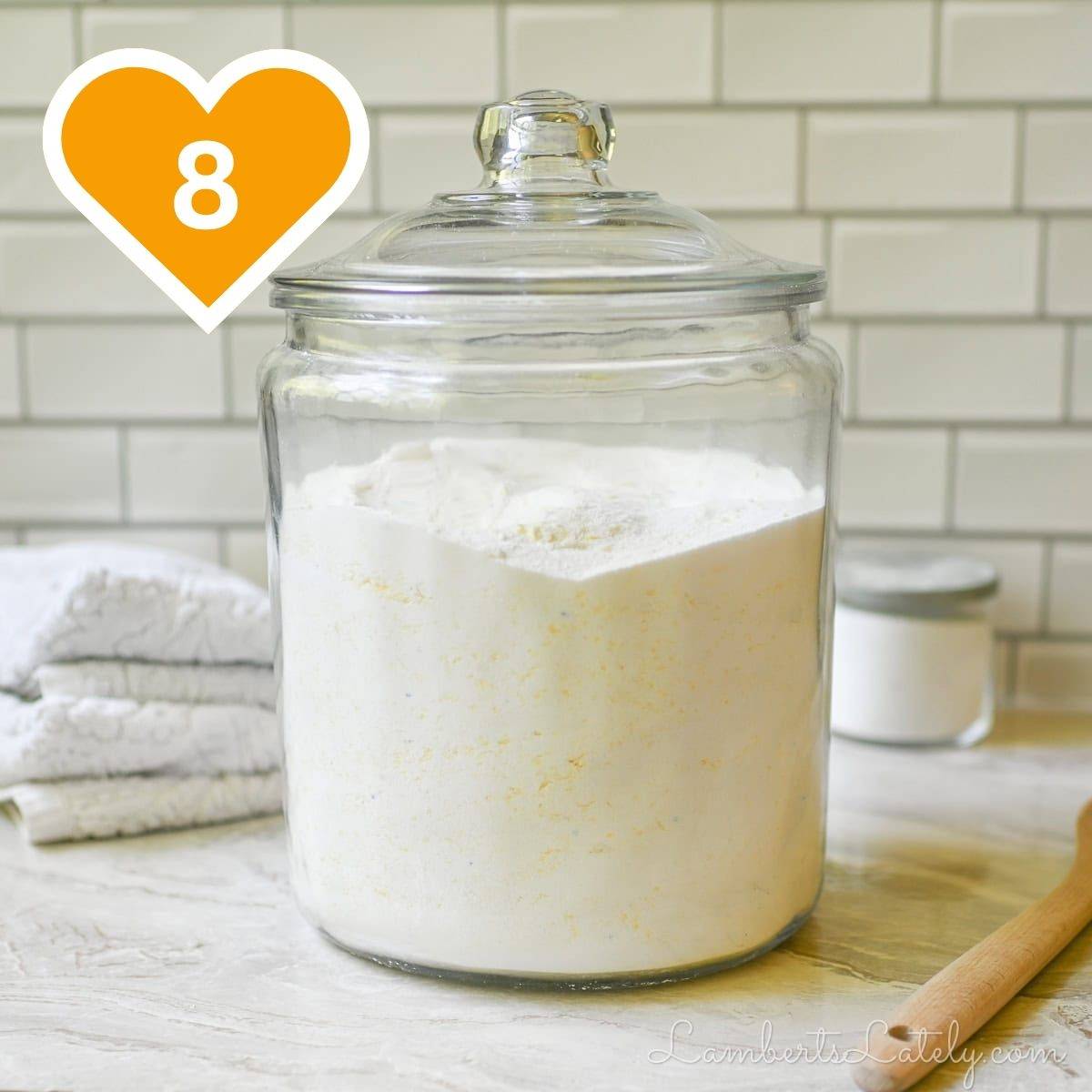Large glass jar filled with homemade powdered laundry detergent on a laundry room counter.