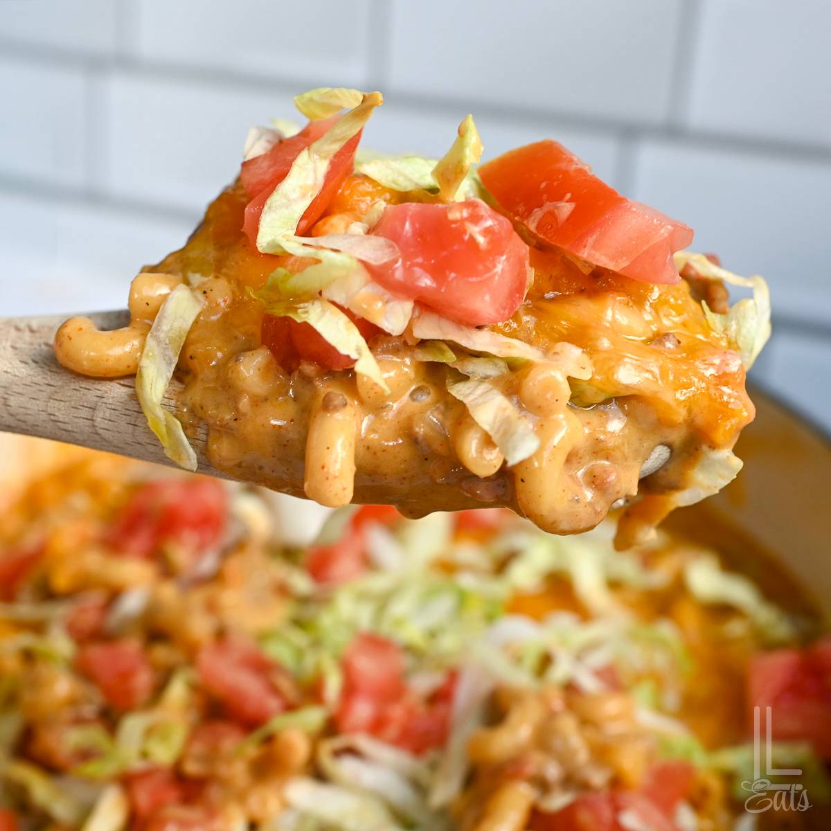 taco mac and cheese topped with lettuce and tomato on a spoon.