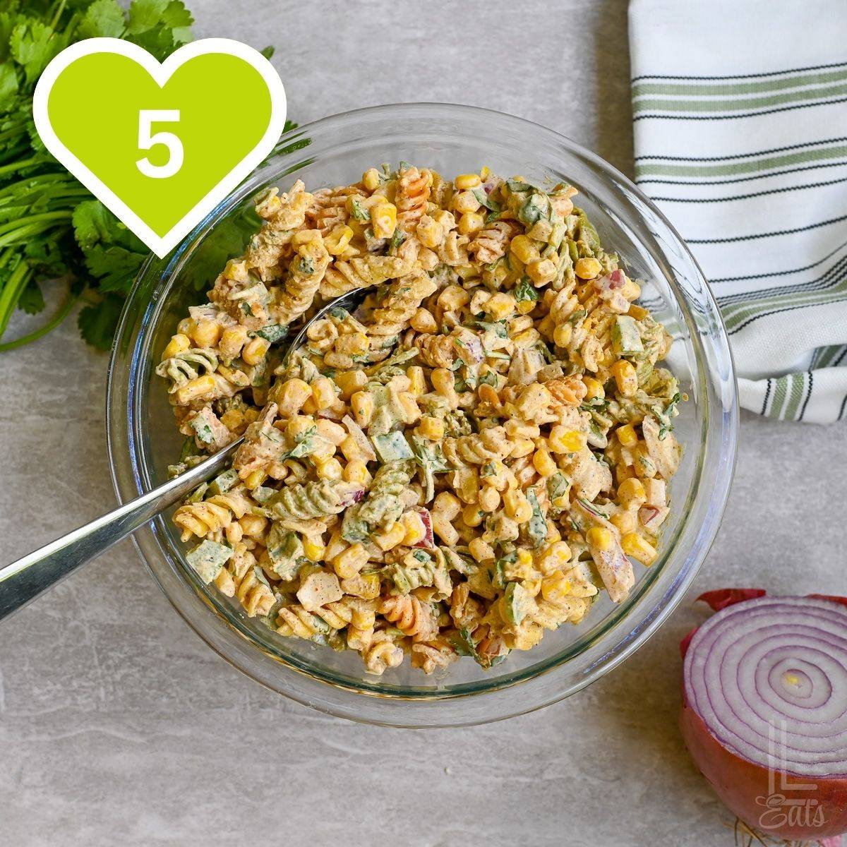 Overhead view of a glass bowl filled with elote pasta salad with herbs and fresh ingredients.