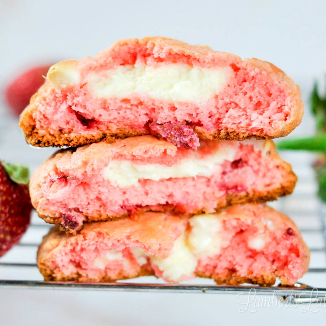A stack of three halved strawberry cookies on a wire rack, showing a soft pink exterior and a thick, creamy white cheesecake filling in the center.