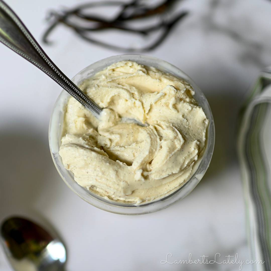 An overhead shot of a Ninja Creami container filled with thick, swirled vanilla bean ice cream with a silver spoon resting inside.