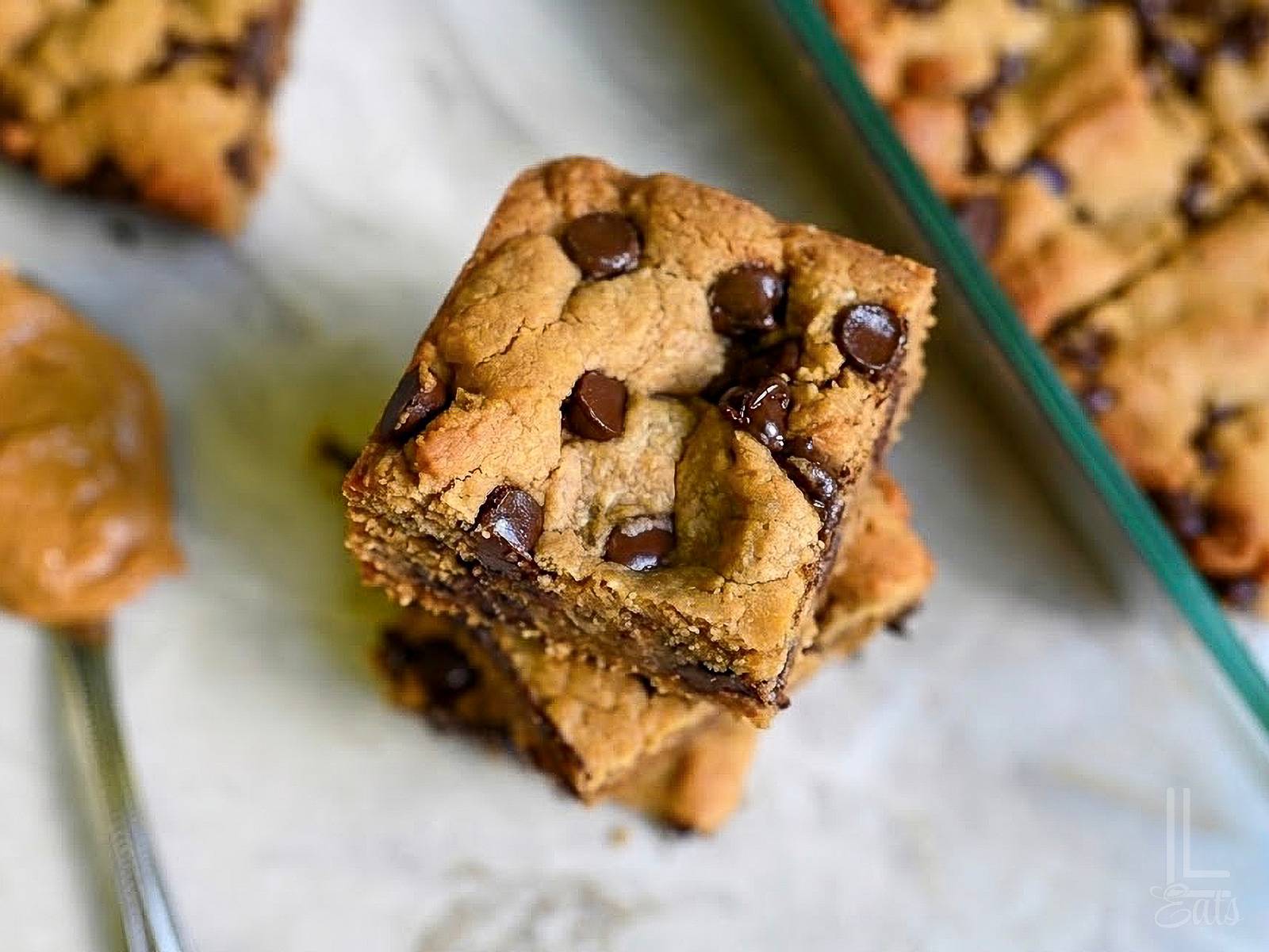 peanut butter cookie bars with chocolate chips in a stack, next to a baking dish.