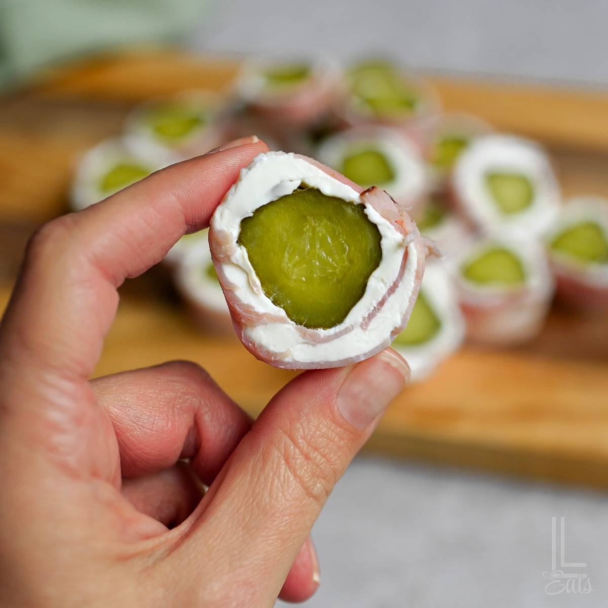 holding a pickle roll up with cream cheese and ham.
