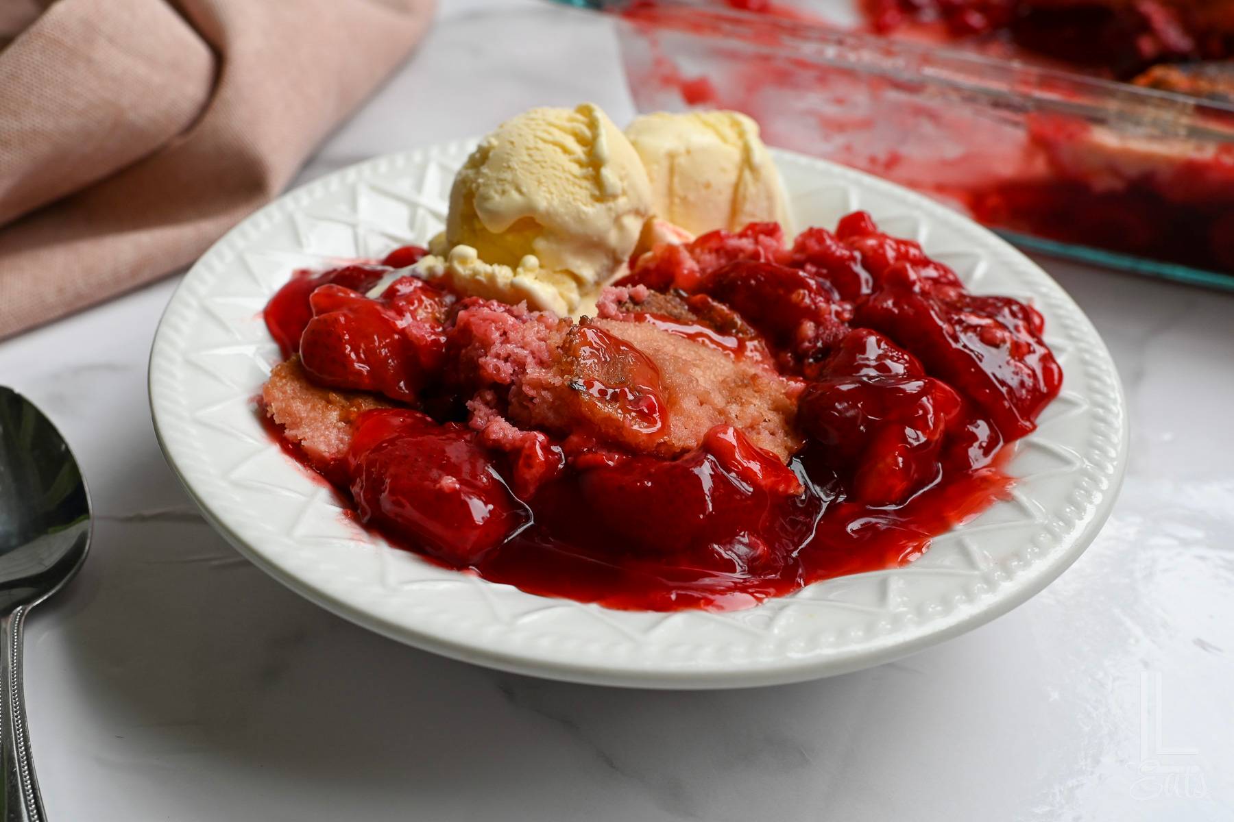 strawberry dump cake in a bowl with ice cream.