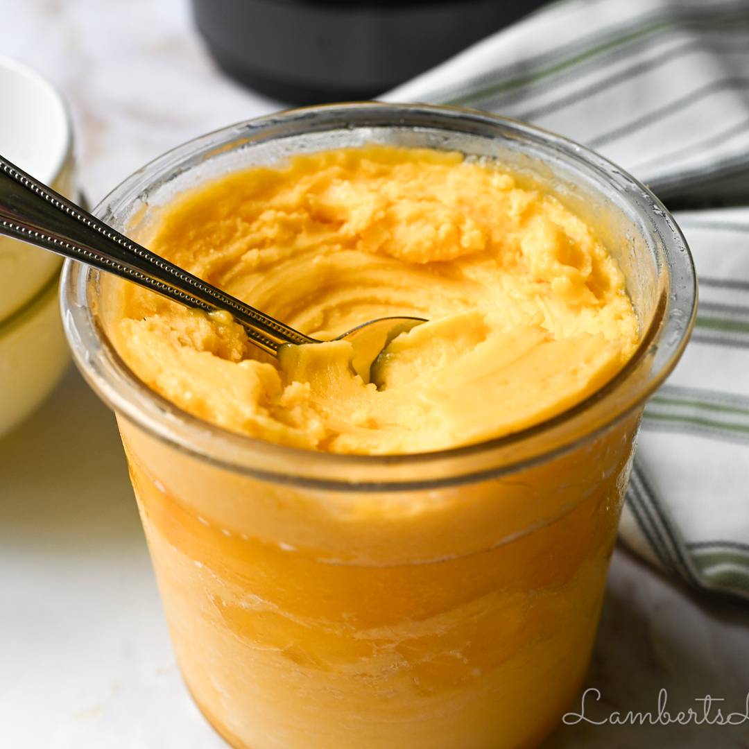 A close-up of a clear Ninja Creami container filled with bright orange mango sorbet, showing a smooth and creamy frozen texture.