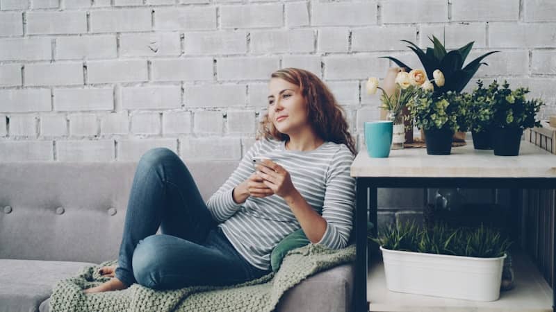 Woman relaxing on sofa with phone and coffee.