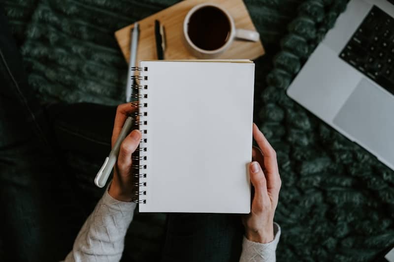 Hands holding a blank notebook with coffee and laptop