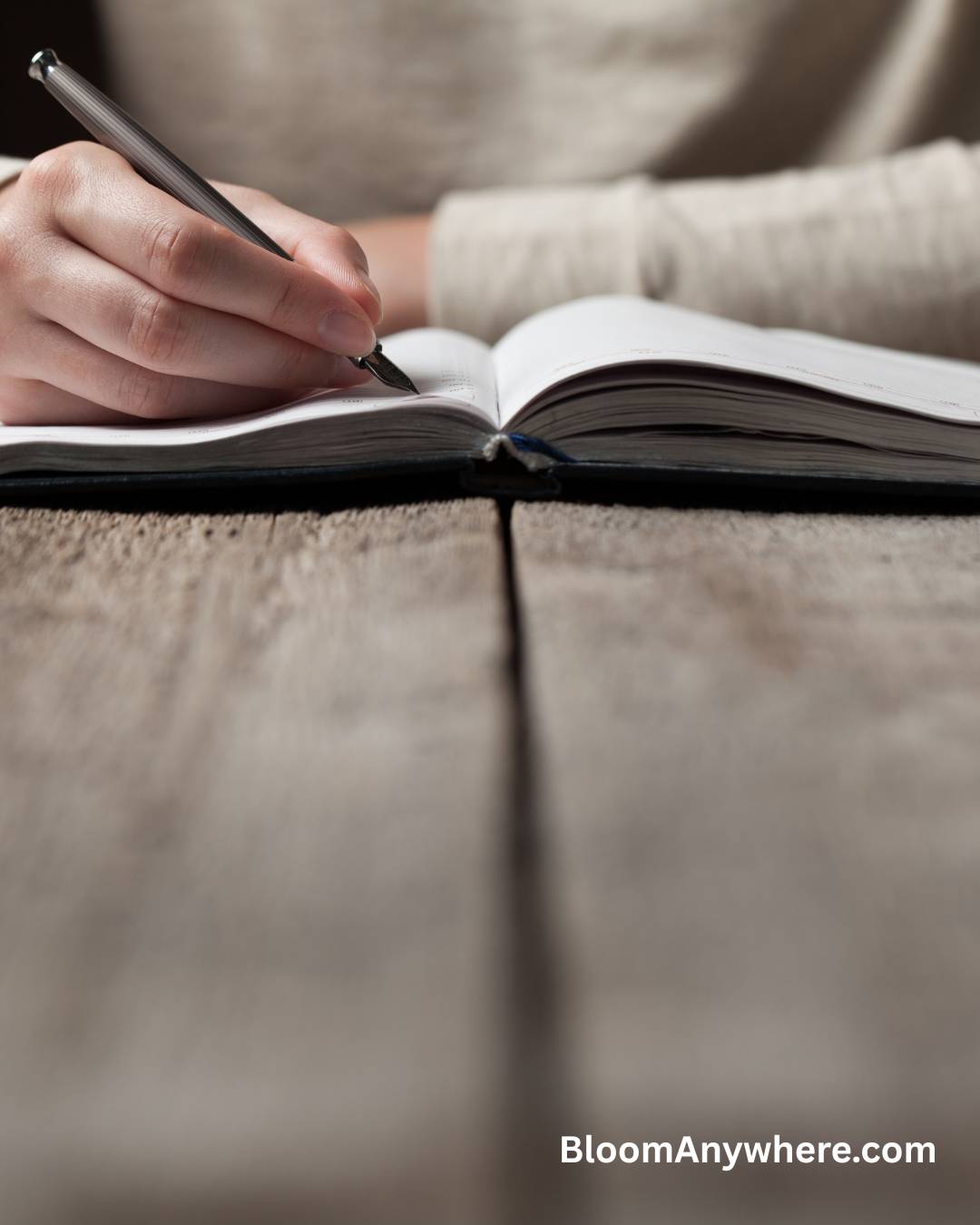 A photo of a woman writing in a notebook on a wooden table.