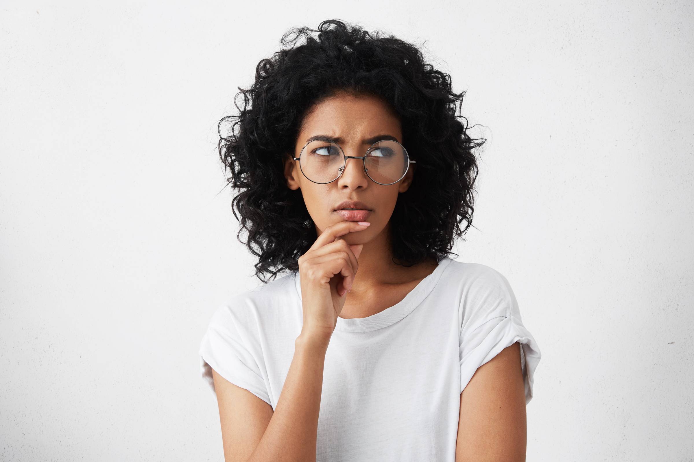 A woman in a white t-shirt and glasses, looking deep in thought.