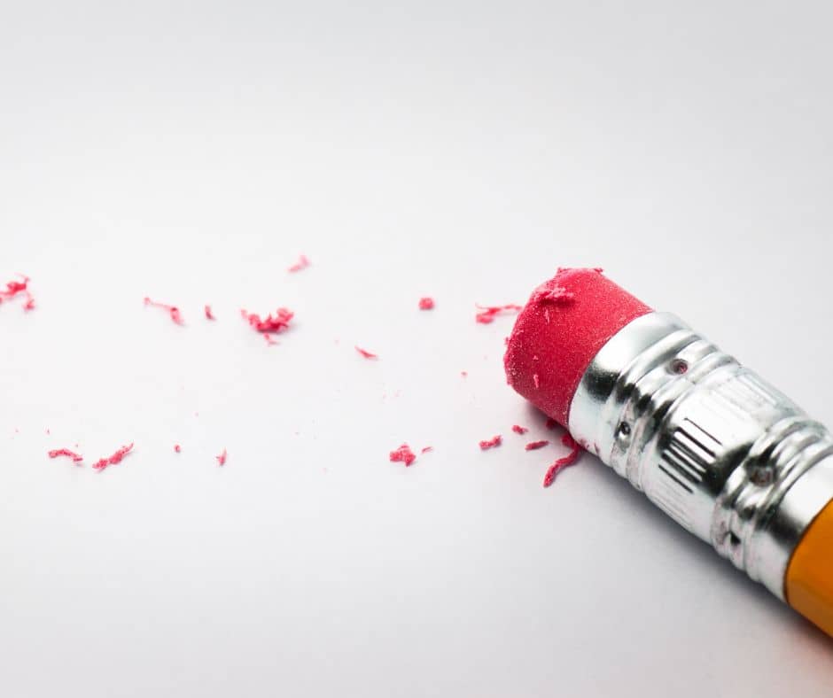 Photo of a pencil with a pink eraser and some of the remnants of the eraser on a white and grey background