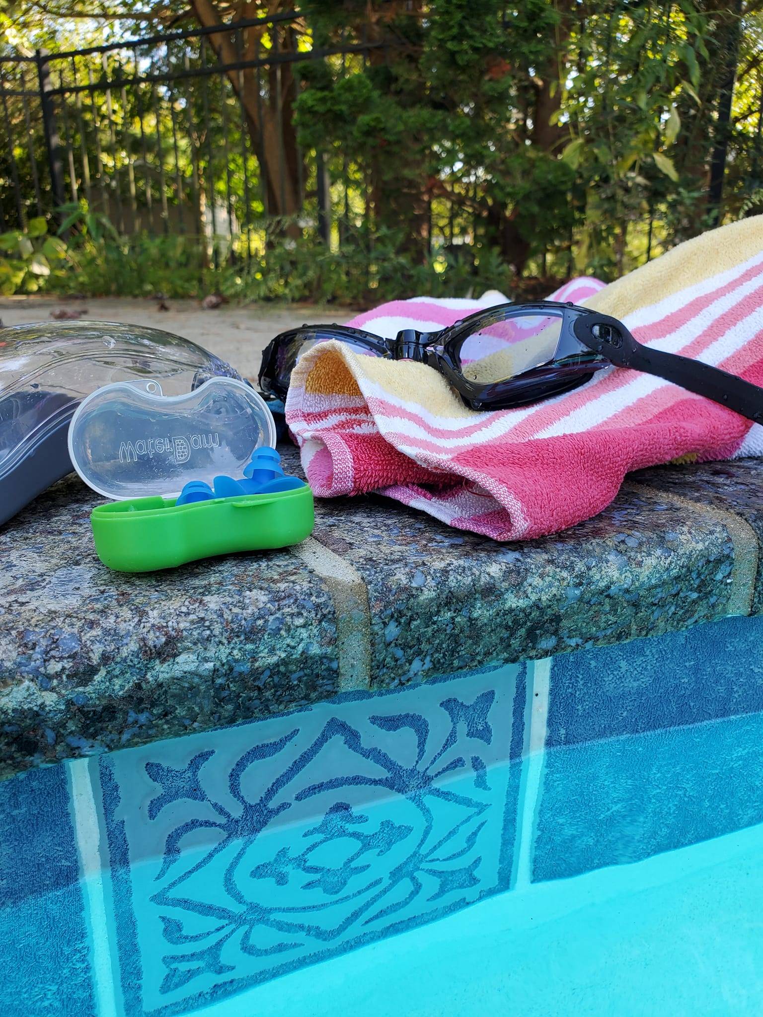 Goggles, towel, and ear plugs sitting on the concrete side of an inground pool