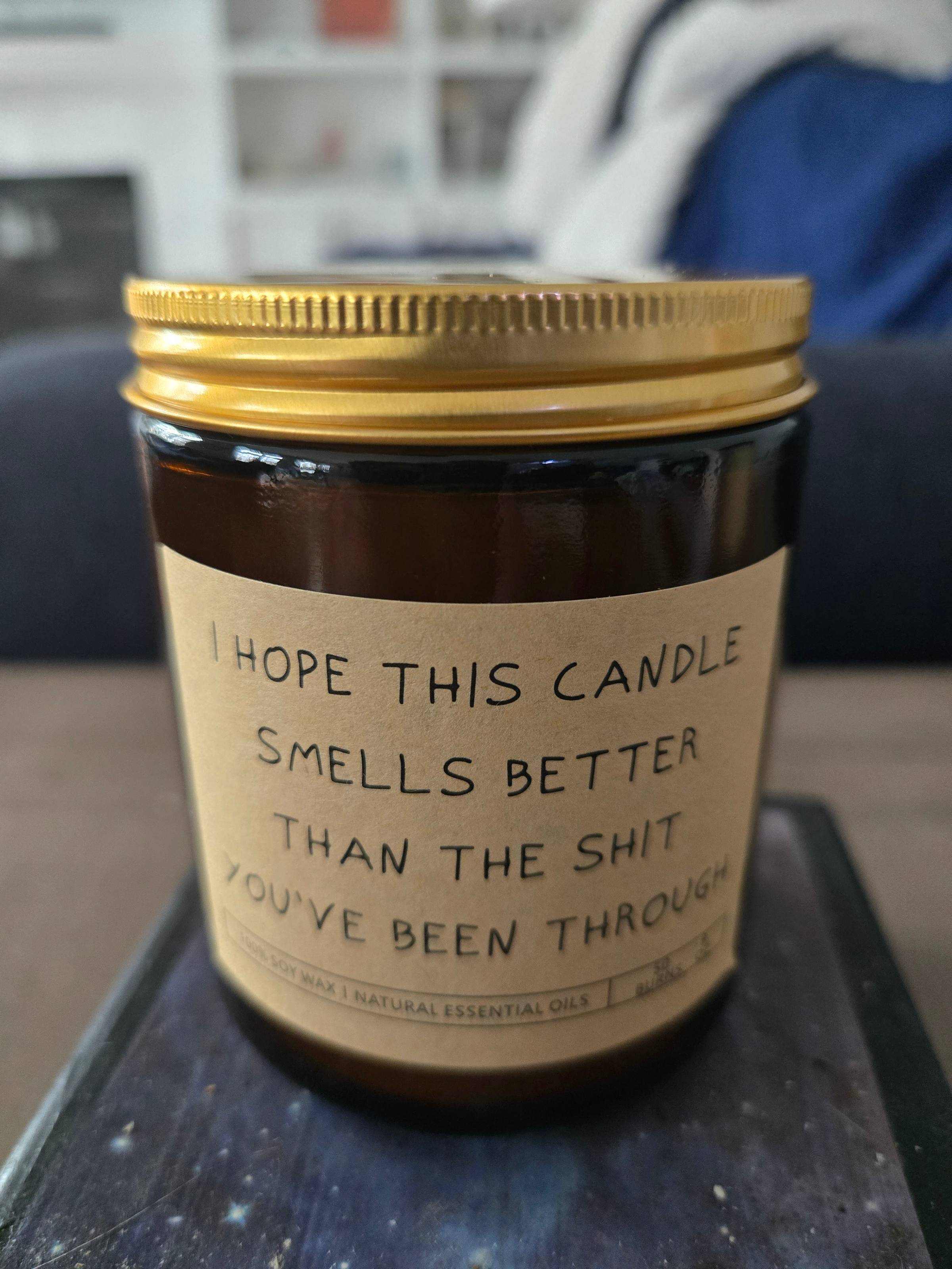 A brown candle in a jar with the label "I hope this candle smells better than the shit you've been through."