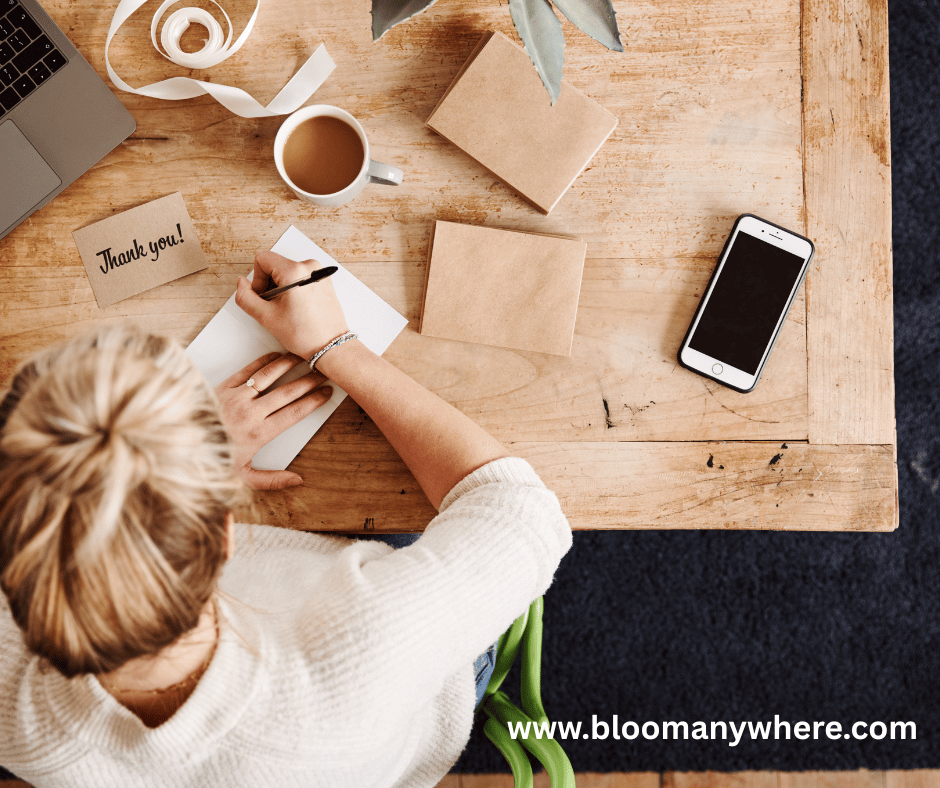 Overview shot of a blonde woman sitting at a table writing a thank-you note.
