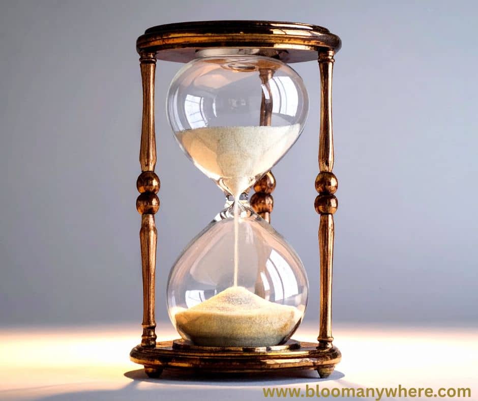 A vintage hourglass with off-white sand inside. The hourglass is bronze against a grey and beige background.