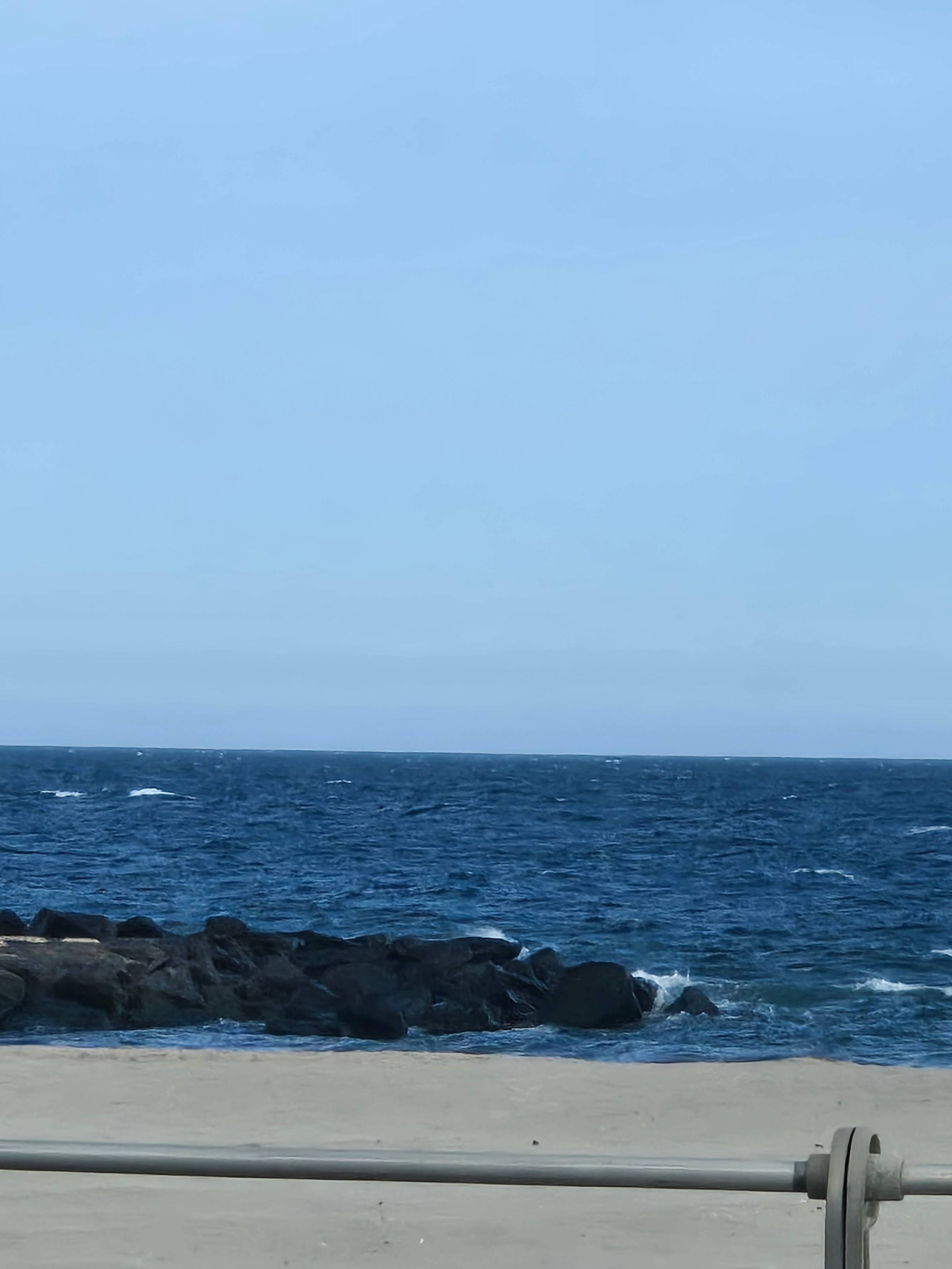 a photograph of the ocean with deep blue water, a light blue sky, and a black jetty