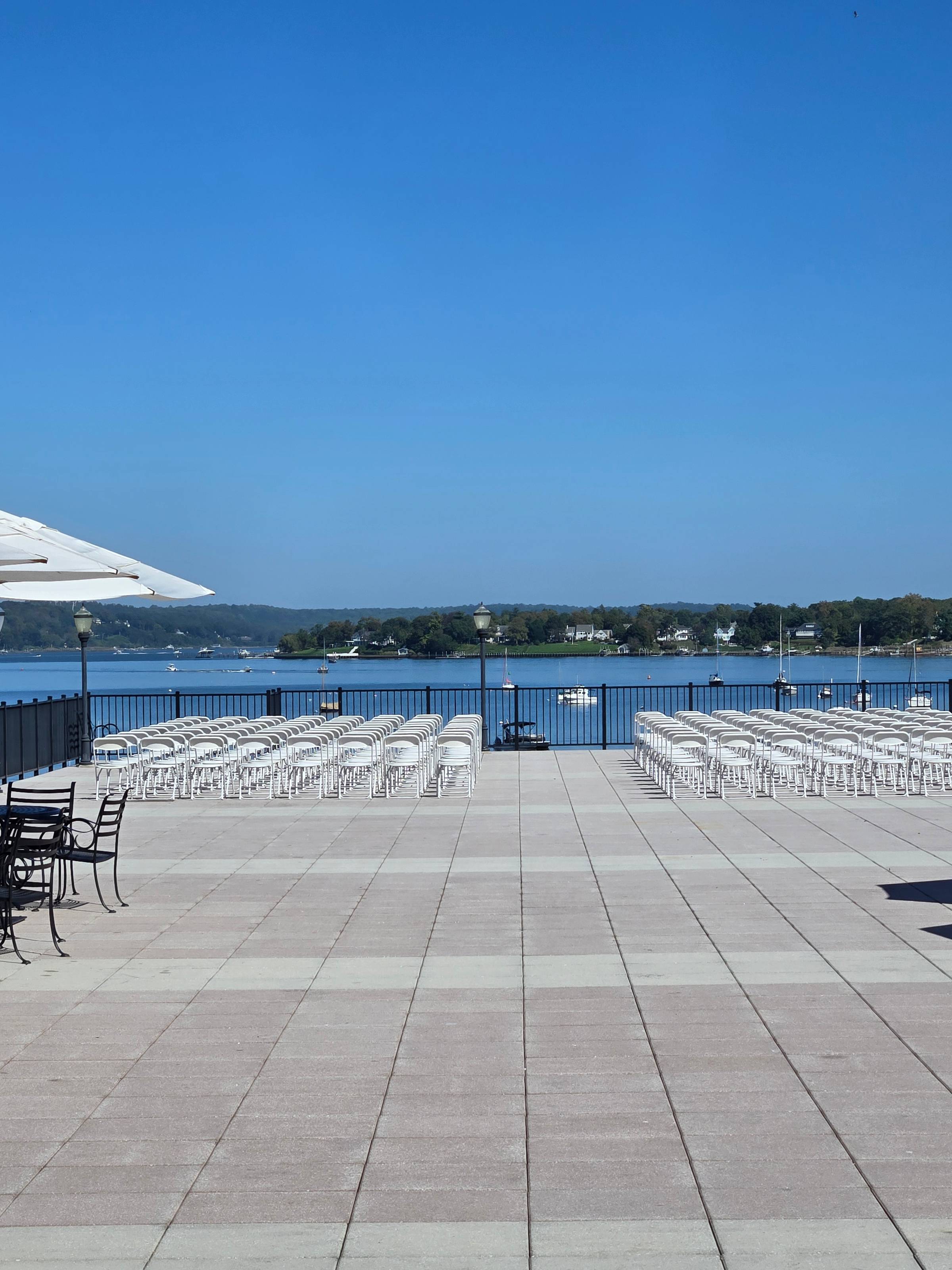 View of a patio with white chairs and a blue sky and river beyond.