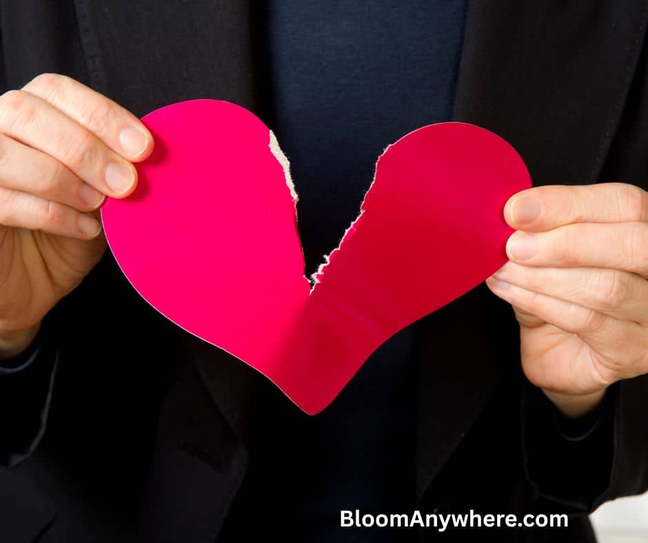 A pair of hands tearing a red paper heart in half. 