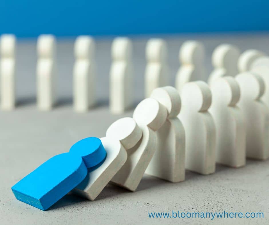 People-shaped dominoes falling. The first one is blue and the rest are white.