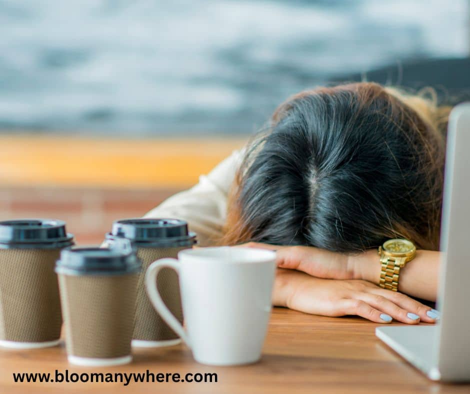 A woman with her head on the desk, old coffee cups in front of her.