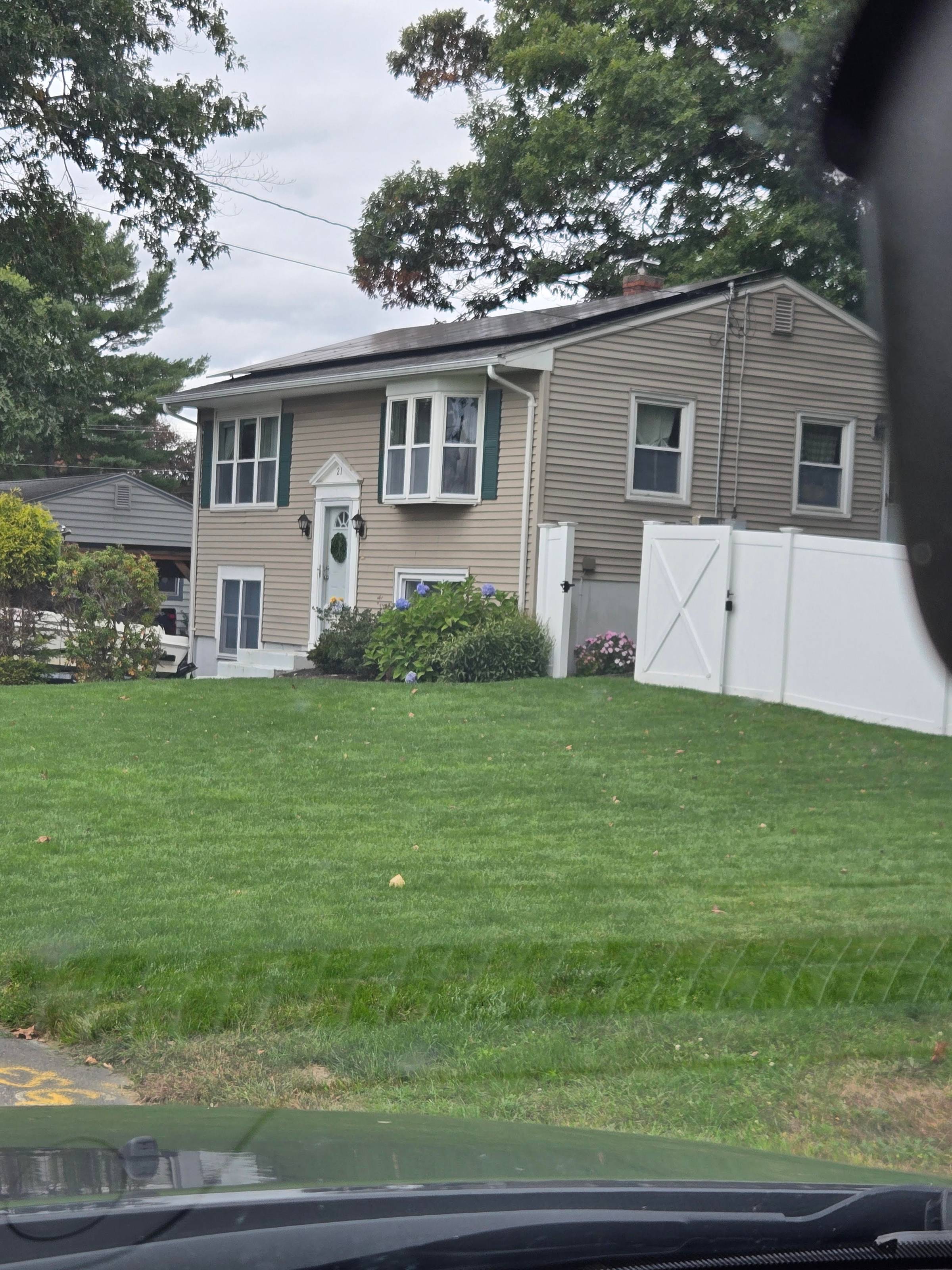 Photo of a taupe house, green lawn and white fence