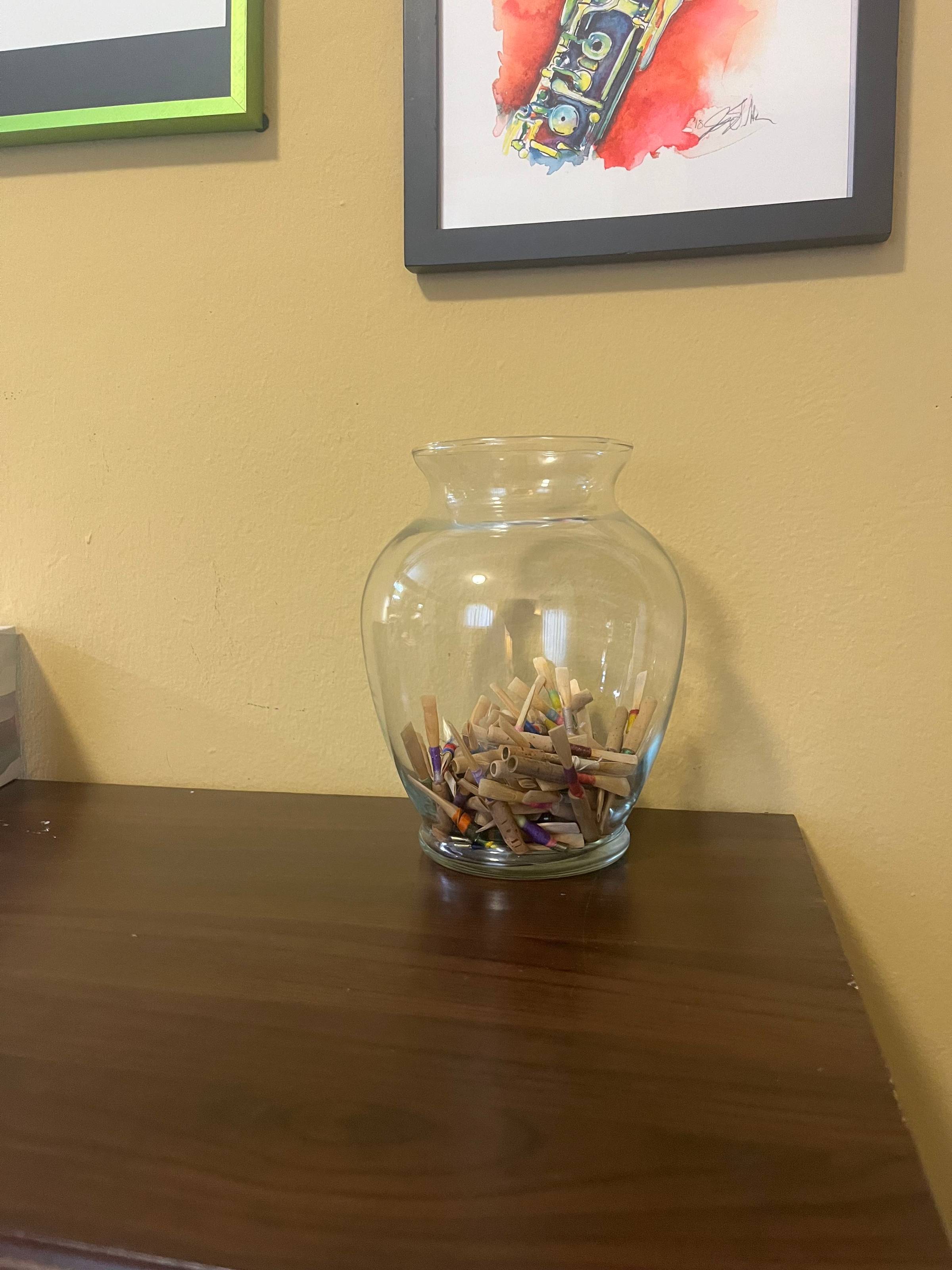 Glass jar with used oboe reeds in it on a wooden table. 