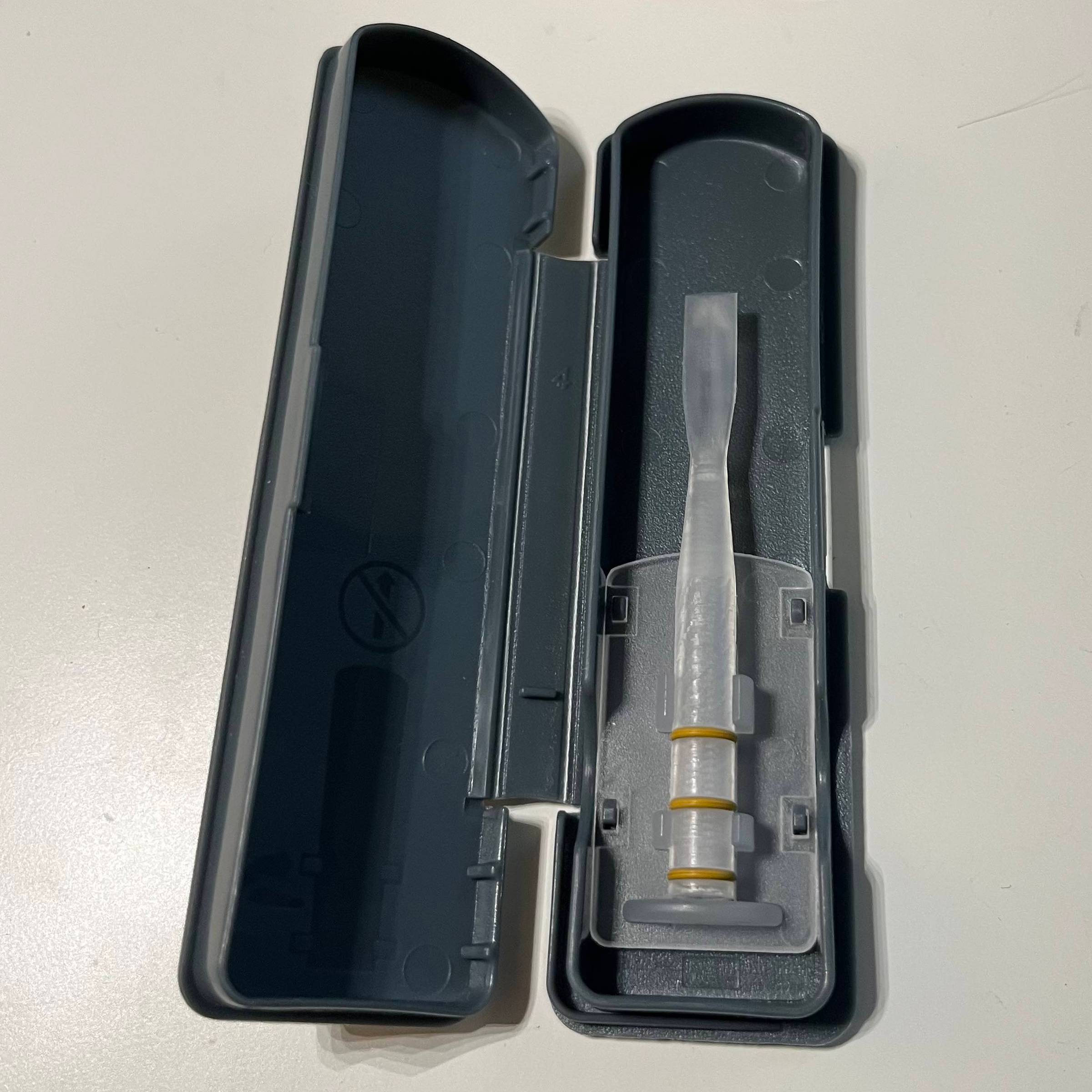 A clear plastic Legere oboe reed with yellow o-rings inside a grey plastic case
