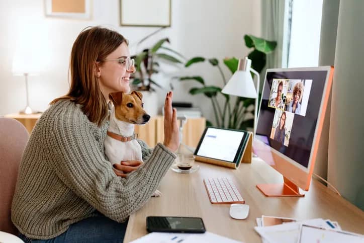 A remote worker holds her dog and waves to her distributed team on Zoom