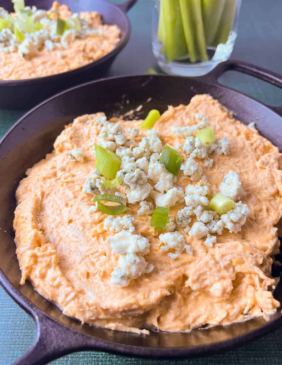 buffalo chicken dip in a cast iron skillet with blue cheese and green onions on top. 