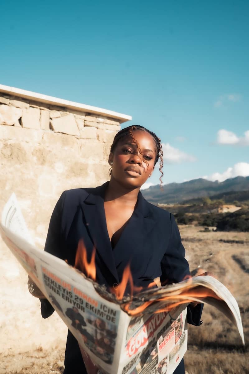 A woman holds a burning newspaper outdoors.