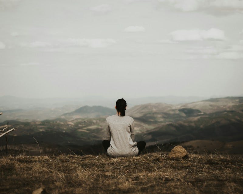 woman sitting on cliff overlooking mountains during daytime