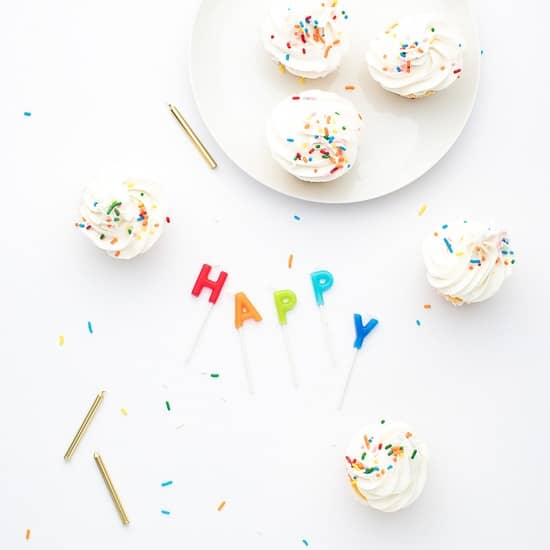 White cupcakes with candles that spell out "happy"