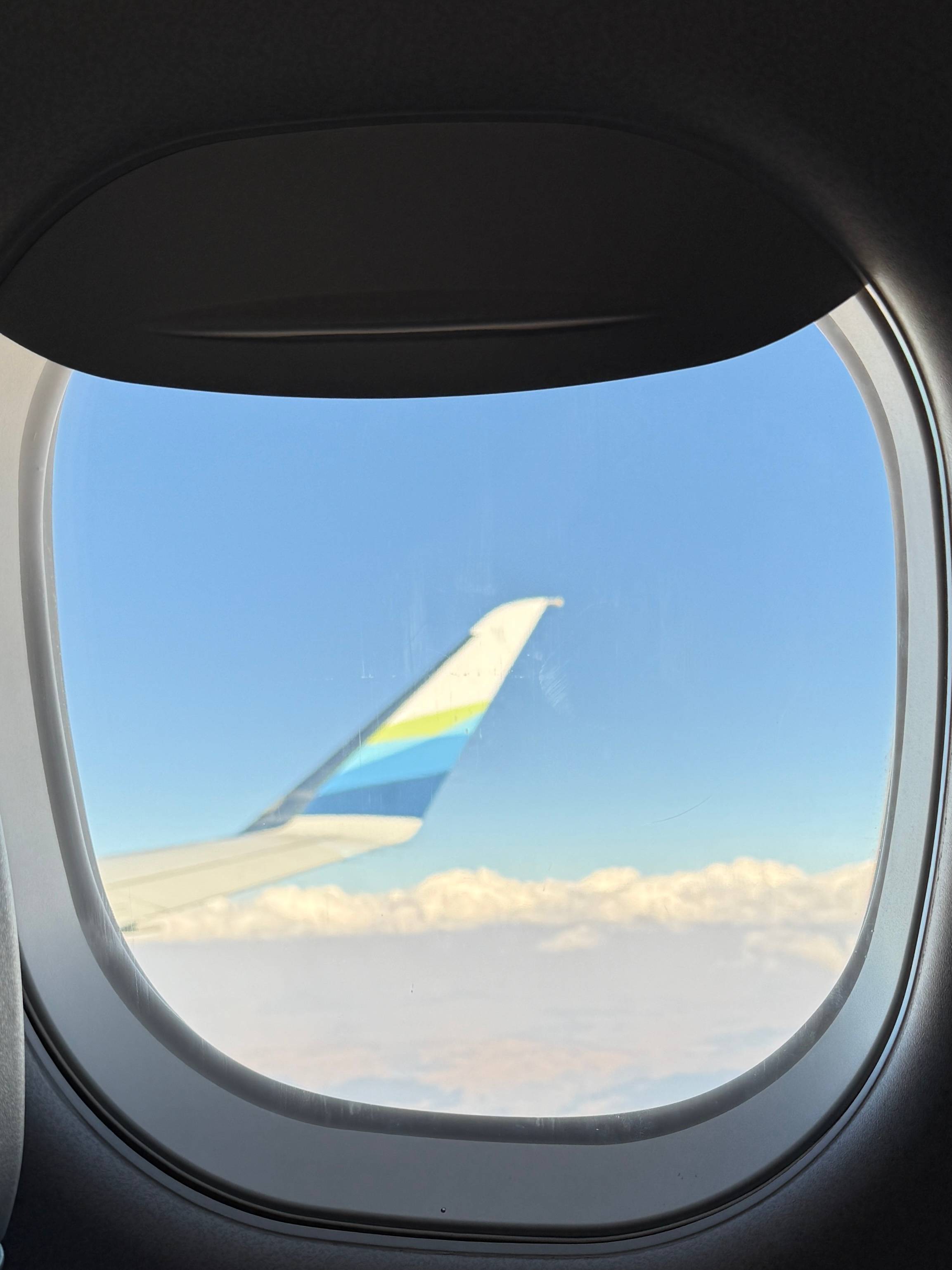 photo taken through the window on Alaskan airlines flight of plane tail against blue sky with clouds at the bottom