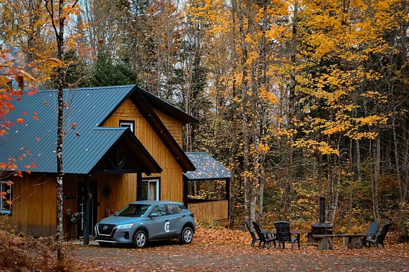 A car parked in front of a cabin in the woods