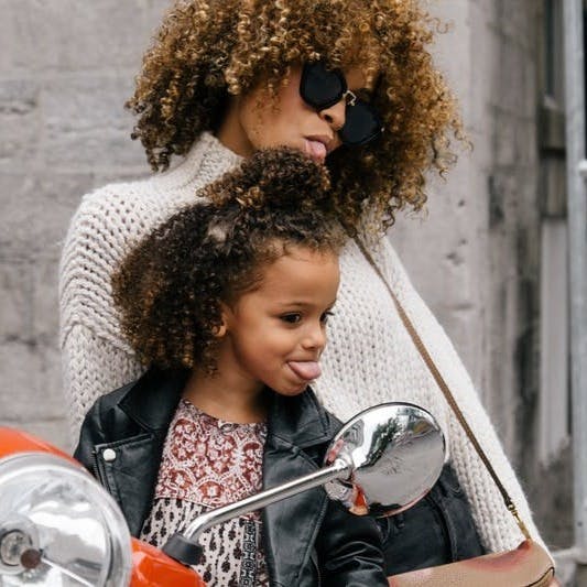 woman and girl showing their tongues beside motorcycle