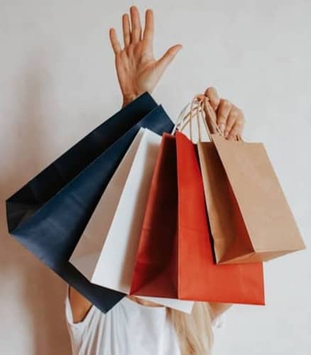 Person holding multiple shopping bags in front of white wall