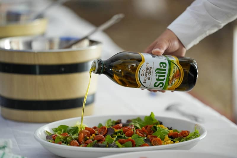 Hand pouring olive oil onto a fresh salad.