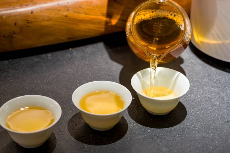 Golden tea pouring from a teapot into small white cups.