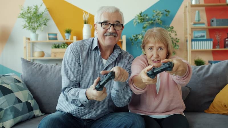 Elderly couple playing video games together on couch.