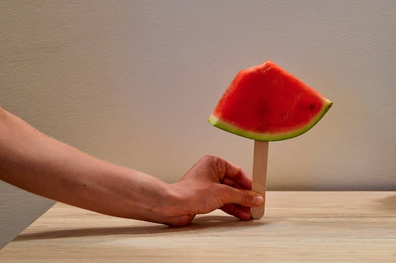 Hand holding a refreshing watermelon slice on a stick.