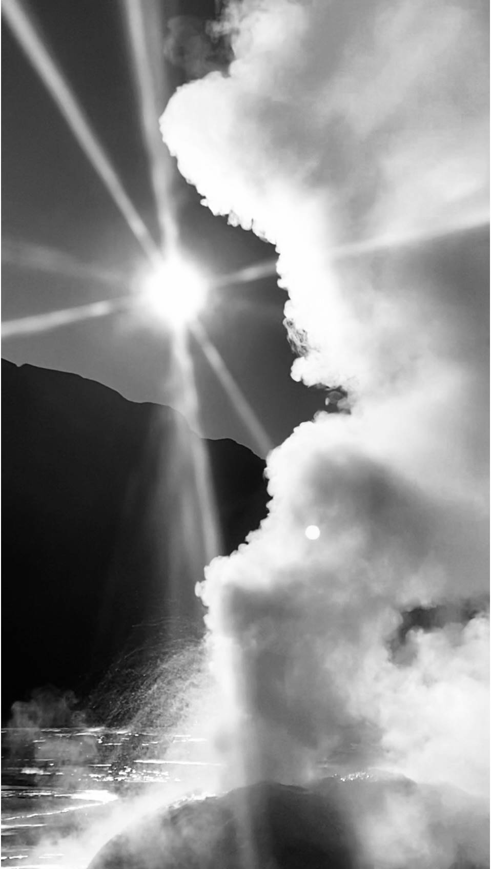 A black and white photo of sunlight piercing through a dense cloud of steam, rising above a geyser field in the Atacama desert in Chile — evoking clarity beyond confusion.