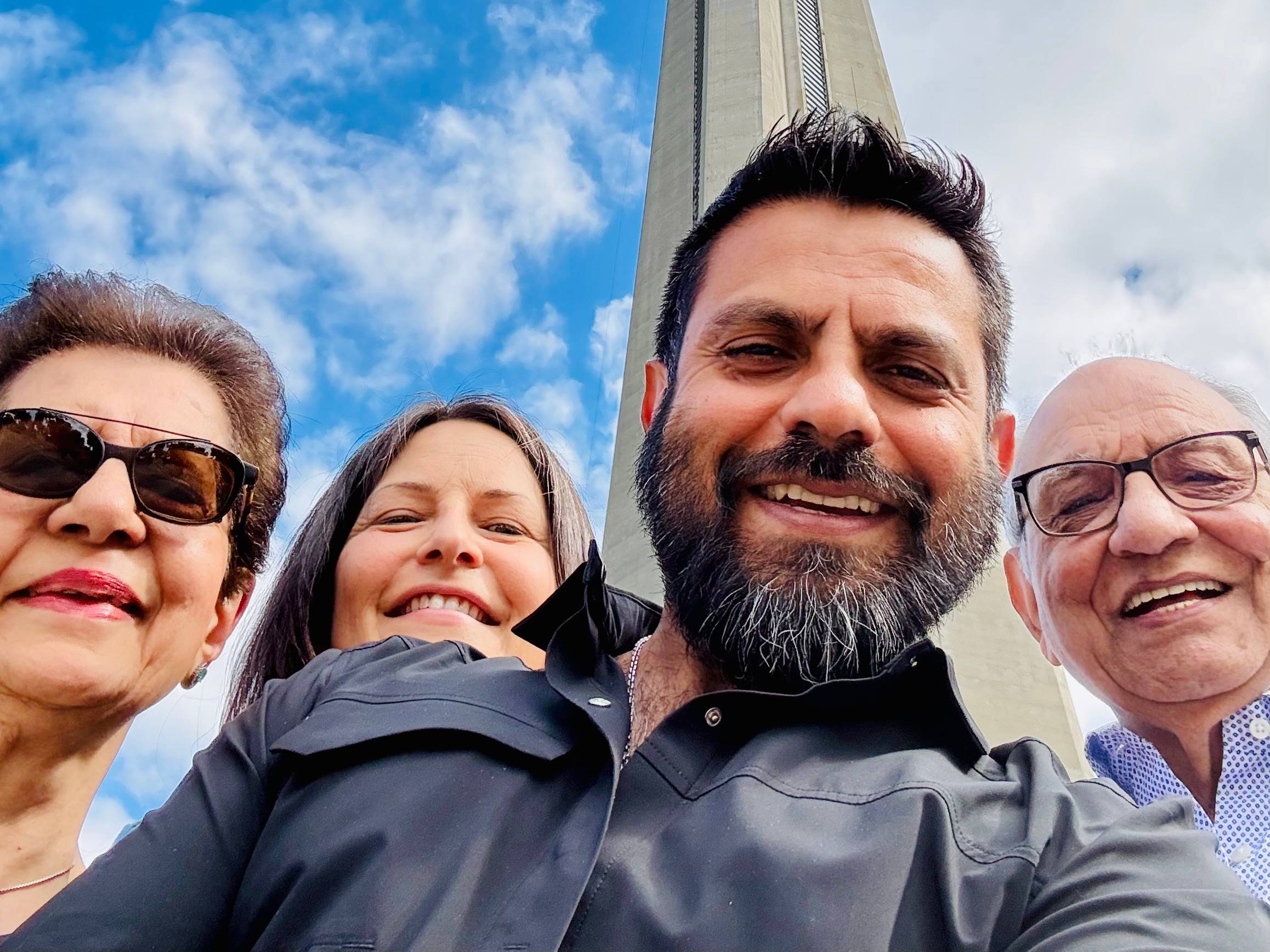 Zaheer standing with his parents and partner beneath the CN Tower in Toronto, all smiling under a bright blue sky.
