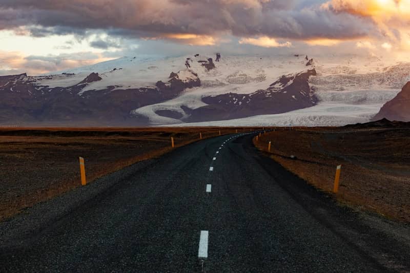 A road stretches toward mountains and a cloudy sky.