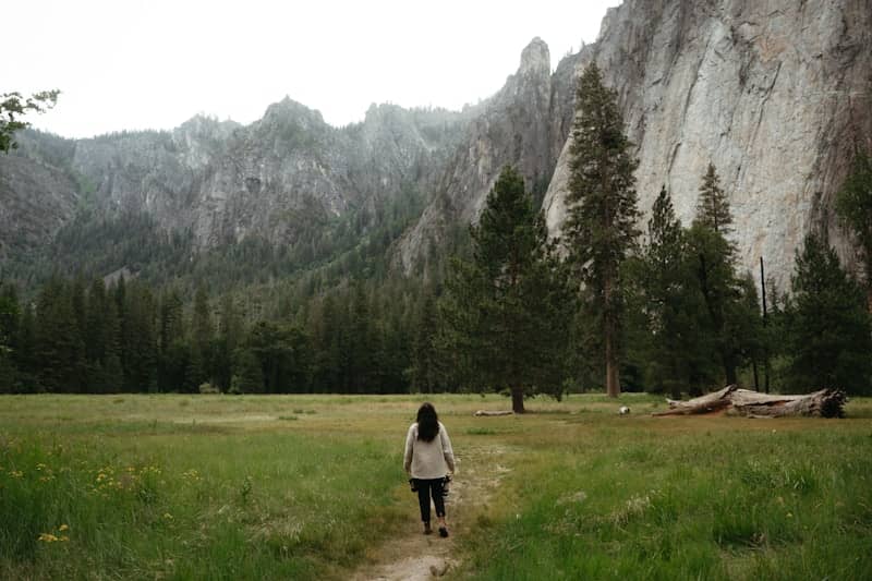 Woman walks through a grassy field towards mountains.