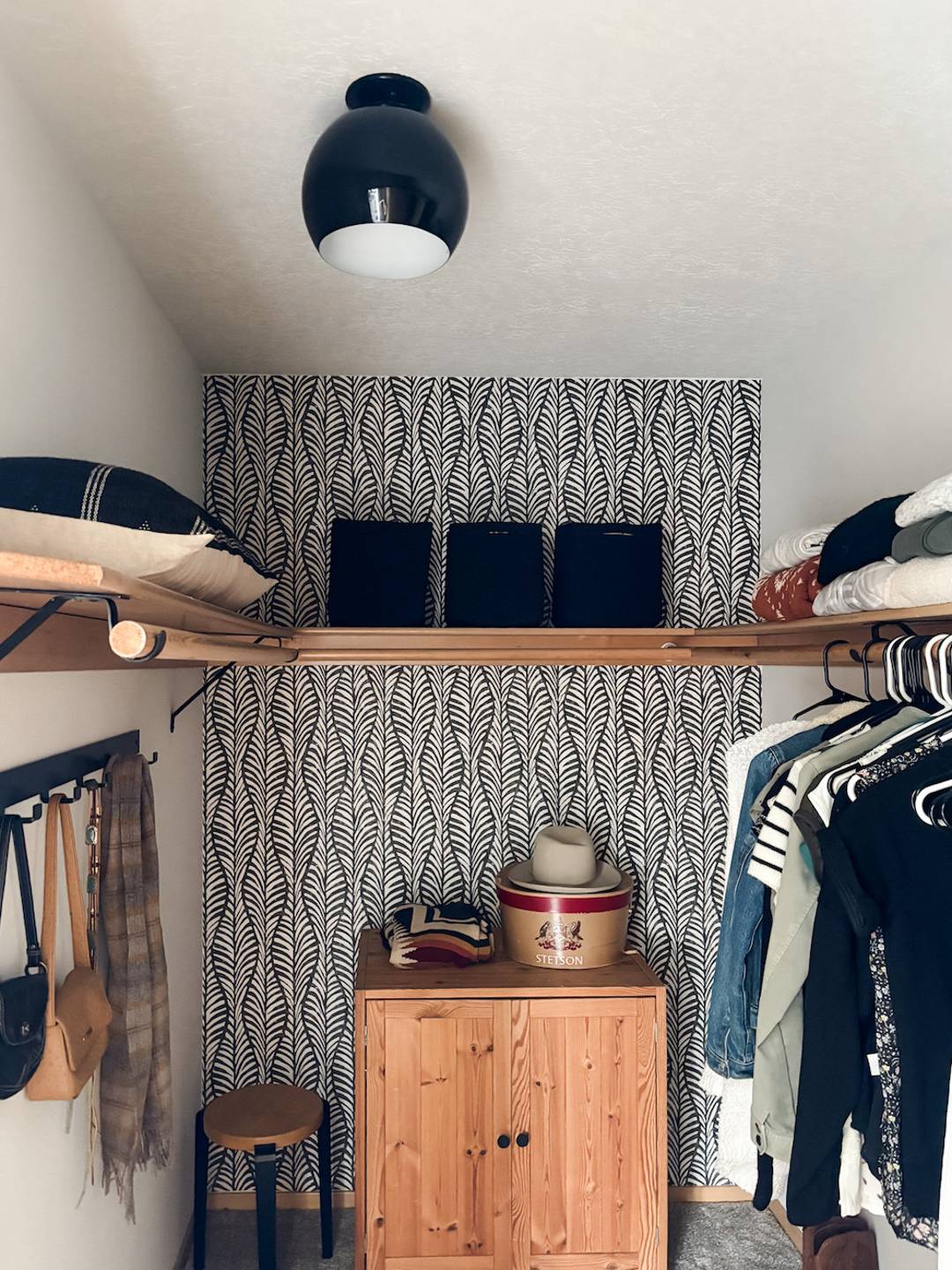 closet with wood shelf, wallpaper, and black light fixture