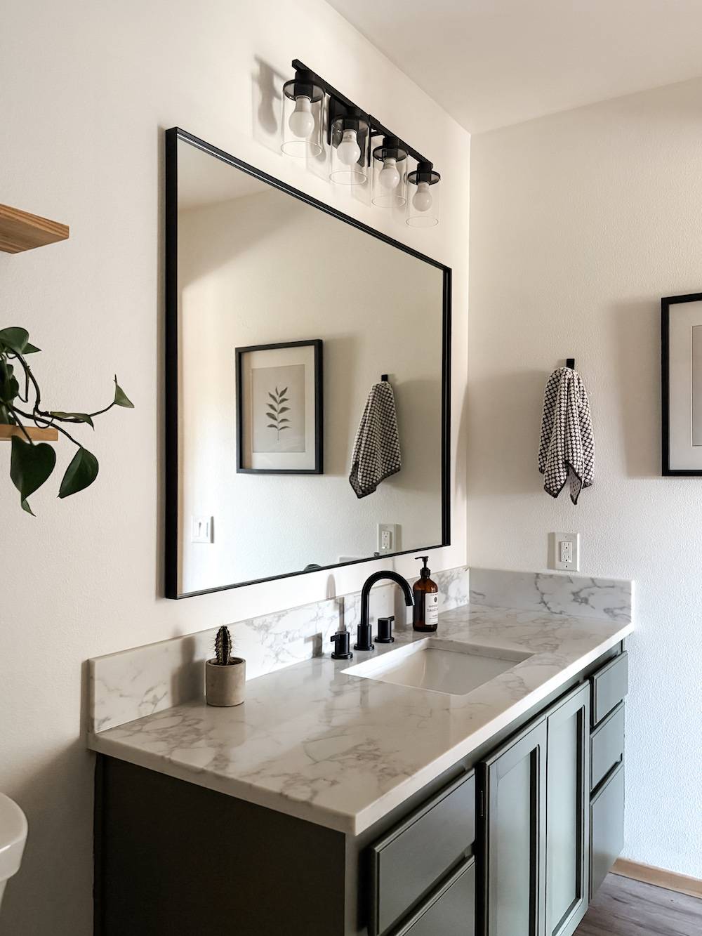 white bathroom with green cabinets, quartz countertops, and black metal mirror