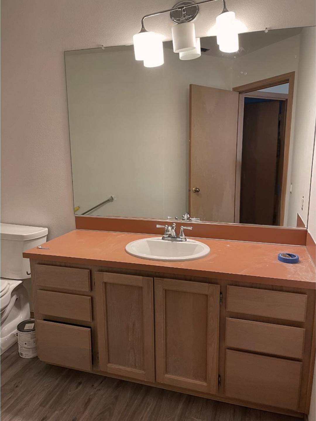 old bathroom with orange countertops, crooked light, builder grade mirror, and peach walls