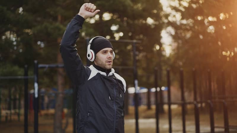 Man in headphones raises fist outdoors.