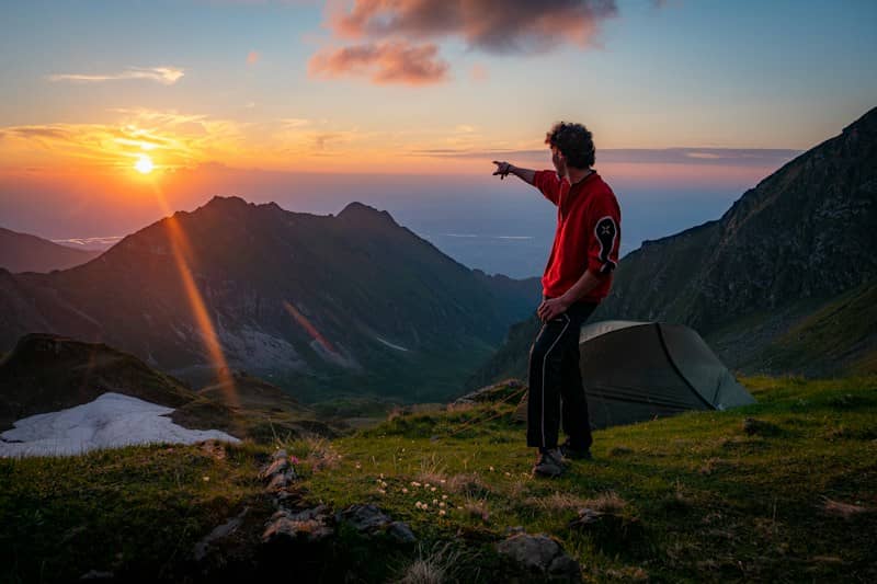 Man points at sunset over mountain landscape with a tent