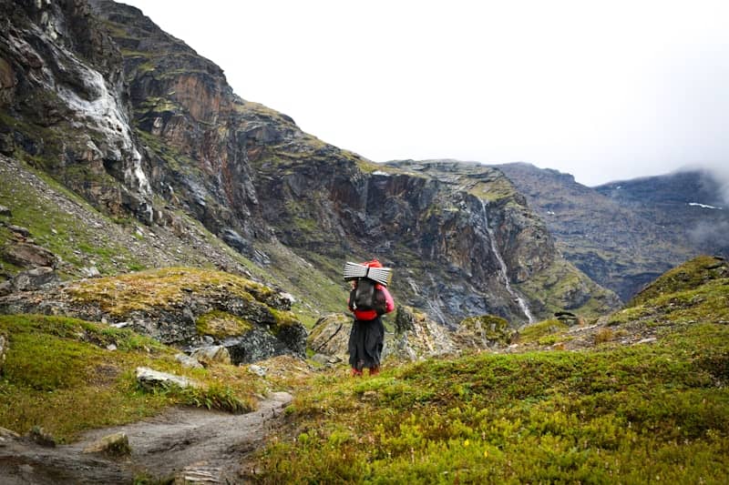 A hiker with a large backpack walking on a trail in a rocky mountain valley